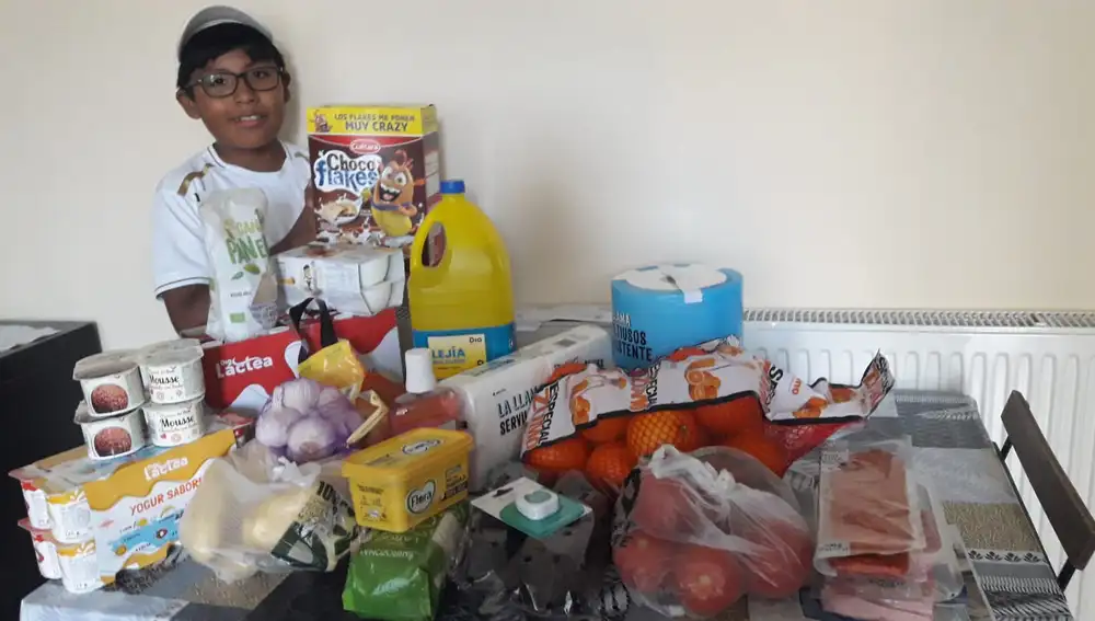 Un niño posa con los productos que sus padres han comprado con la donación de un socio de Cirineo