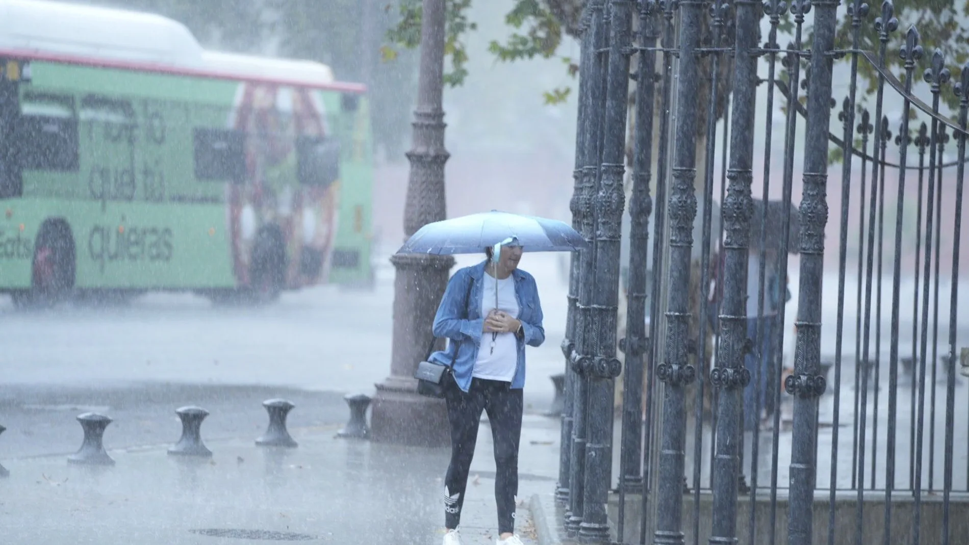 Una mujer camina se cubre de la lluvia con un paragüas