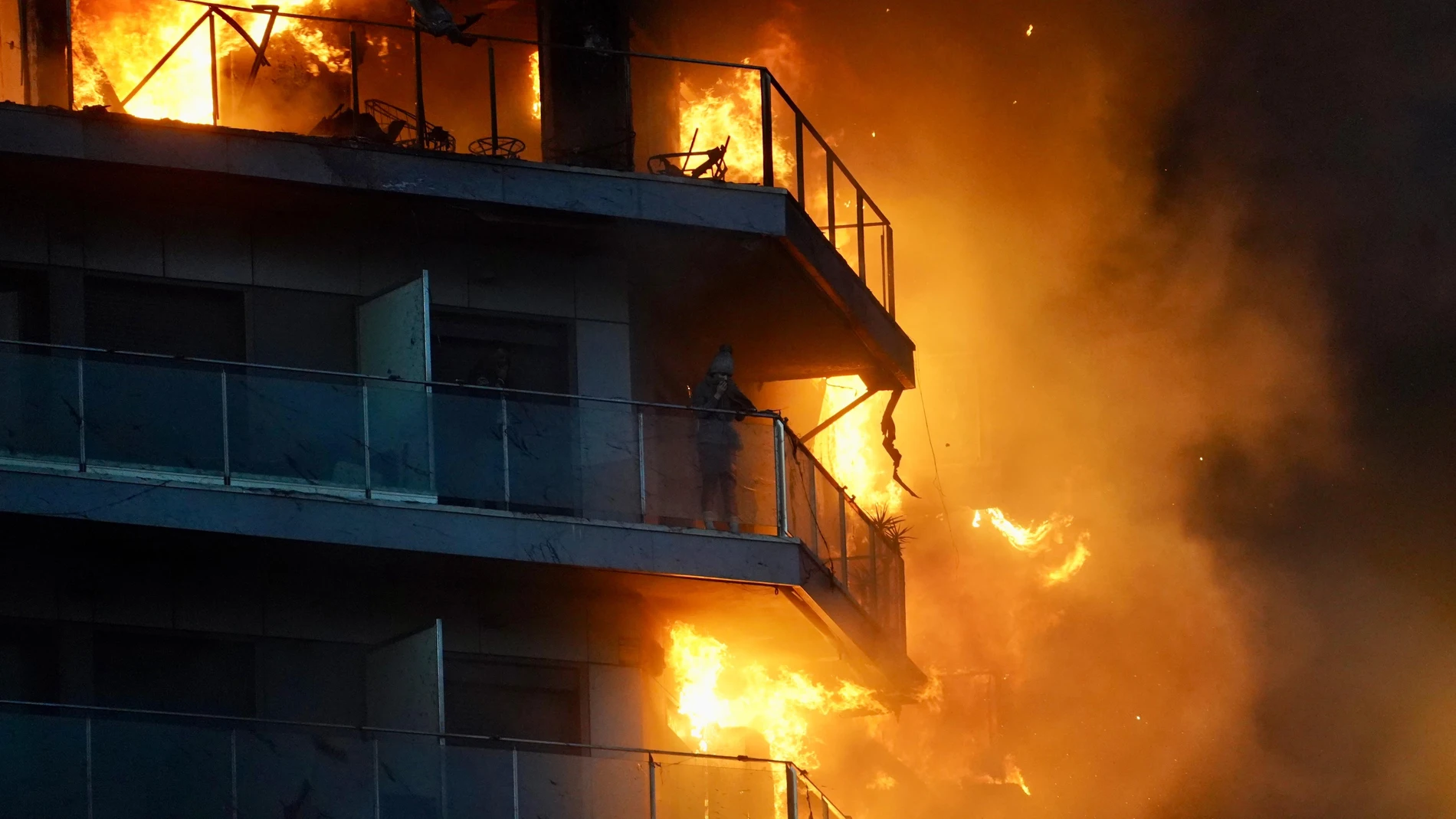 Una persona en un balcón del edificio en llamas, en el barrio de Campanar, a 22 de febrero de 2024, en Valencia, Comunidad Valenciana (España). Un incendio de grandes dimensiones ha arrasado un edificio de 14 plantas en el barrio valenciano de Campanar. El fuego, originado en el cuarto piso del inmueble, ha generado una gran columna de llamas y una densa humareda que ha afectado a varias plantas del edificio. El 112 ha movilizado diez dotaciones de bomberos, dos SAMU y un SVB hasta el lugar d...