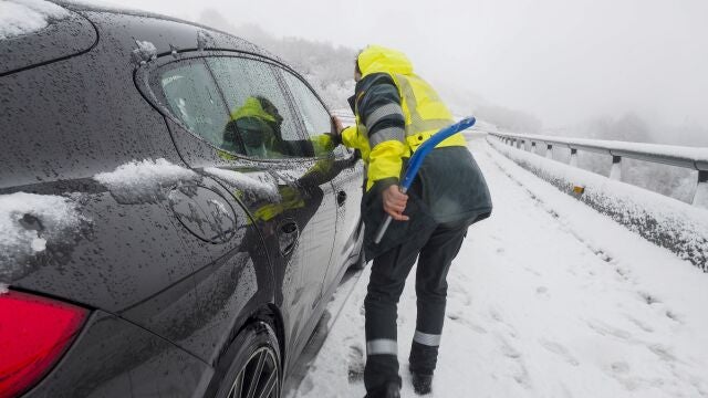 Un agentes de la Guardia Civil auxilia a un vehículo en la Autovía A-6 que se encuentra cubierta de nieve. Carreteras cortadas y cadenas para circular por las nevadas en puertos de montaña del norte especialmente, además de tráfico marítimo suspendido en el Estrecho, olas de 8 metros en el Cantábrico y árboles caídos por la lluvia y el viento son efectos del temporal que un día más mantiene en alerta al país.