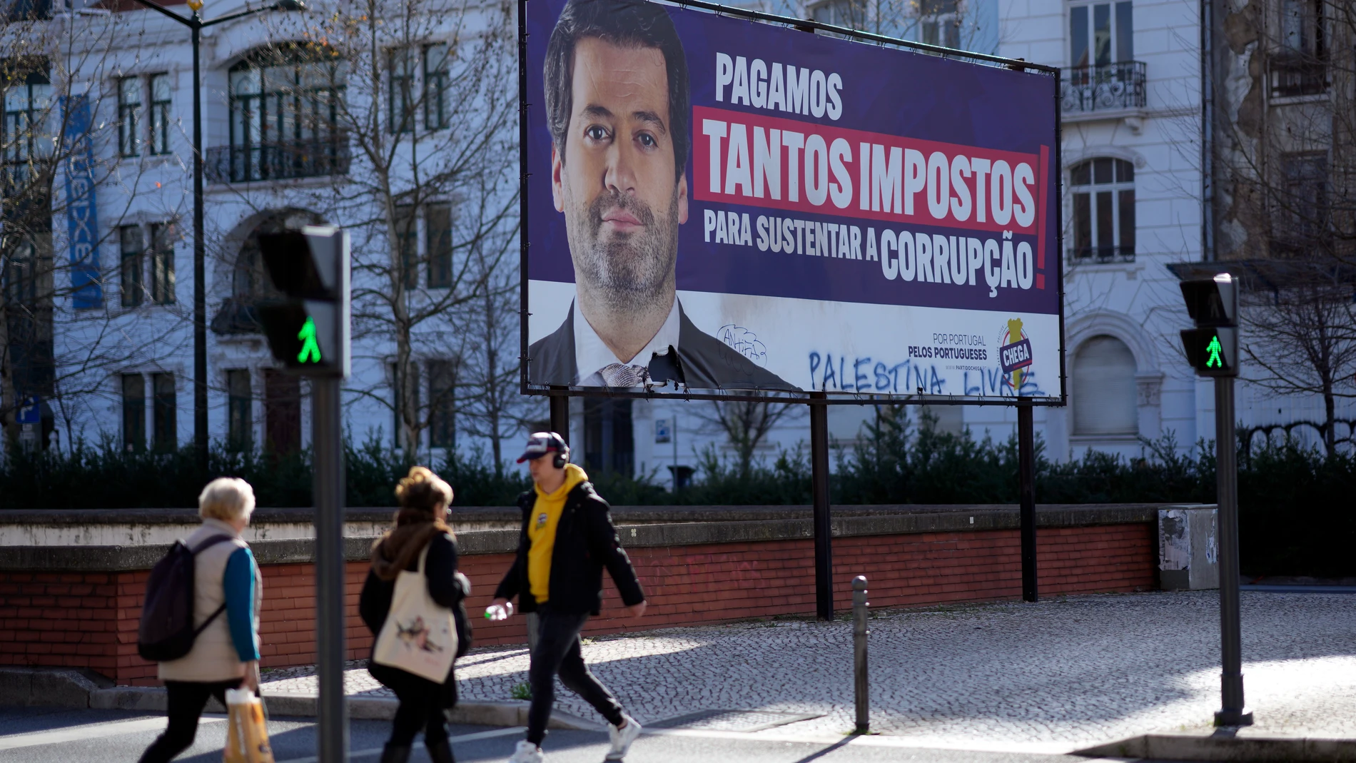 People walk by a billboard for Andre Ventura, leader of populist and nationalist party Chega! (in English, Enough!) with the words, "We pay so many taxes to sustain corruption," in Lisbon, Monday, March 4, 2024. Corruption scandals have cast a shadow over Portugal's March 10 snap election. They have also fed public disenchantment with the country's political class. (AP Photo/Armando Franca)