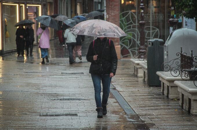 Varias personas pasean bajo la lluvia por el centro de Sevilla