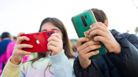 Una niña y un niño con sus móviles
