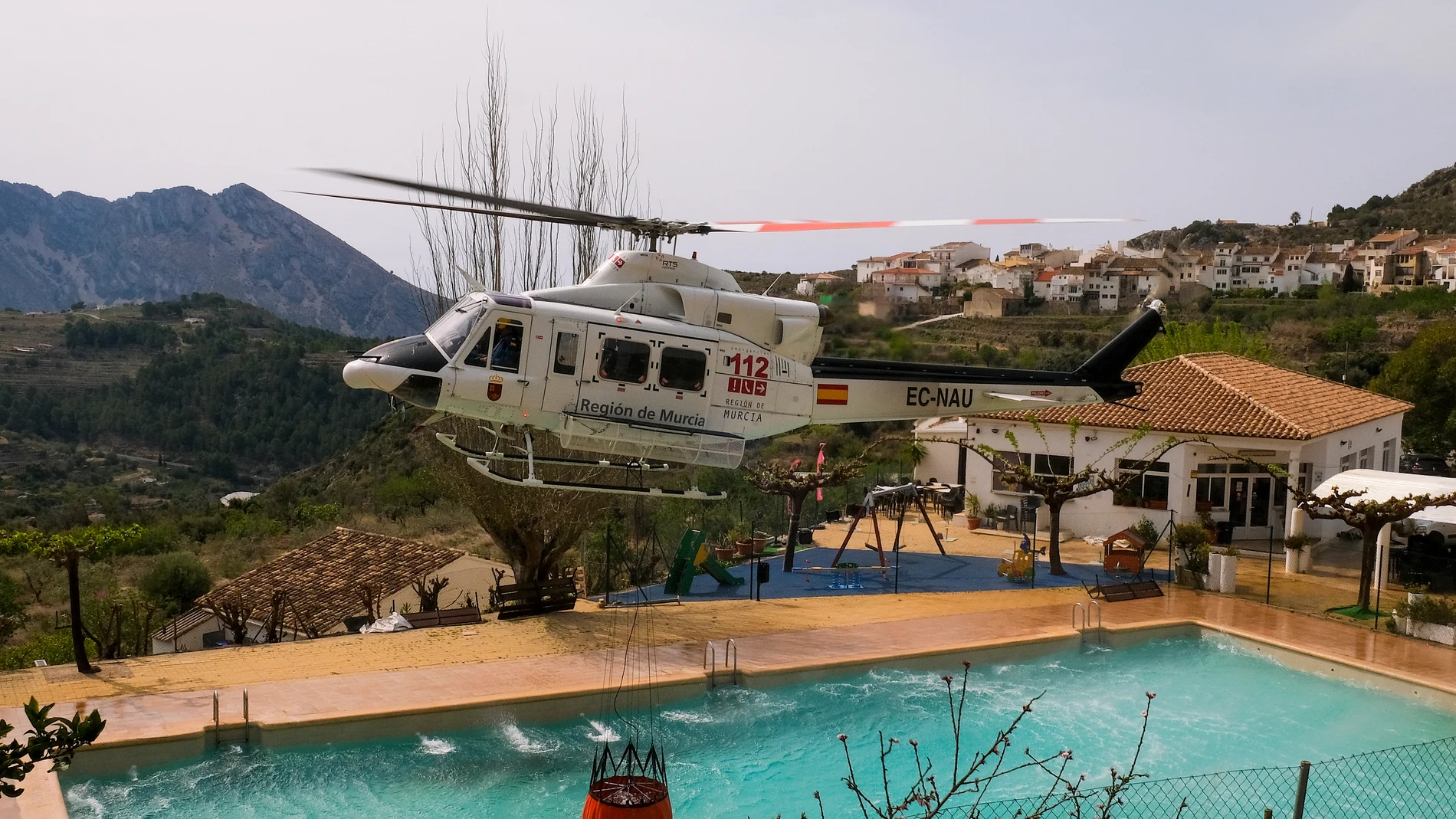 Un helicóptero de los Servicios de Emergencia carga agua en una piscina durante los trabajos de extinción del incendio forestal de Tárbena