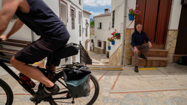 El alcalde de Benarrabá, Silvestre Barroso (d) observando el paso de un cicloturista un pueblo de unos 450 habitantes situado en el Valle del Genal