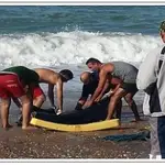 Varias personas recoger el cadáver de un inmigrante ahogado en el mar