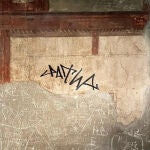 Un turista garabatea su firma con rotulador en una pared con frescos en antigua Herculano