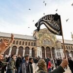 A Syrian rebel fighter holds an Islamist black flag depicting the Islamic Shahada (the creed stating a belief in one god and the acceptance that Mohammed was God's prophet), while walking in the courtyard of the 8th-century Umayyad Mosque in Damascus on December 10, 2024. - Islamist-led rebels took Damascus in a lightning offensive on December 8, ousting president Bashar al-Assad and ending five decades of Baath rule in Syria. (Photo by LOUAI BESHARA / AFP)