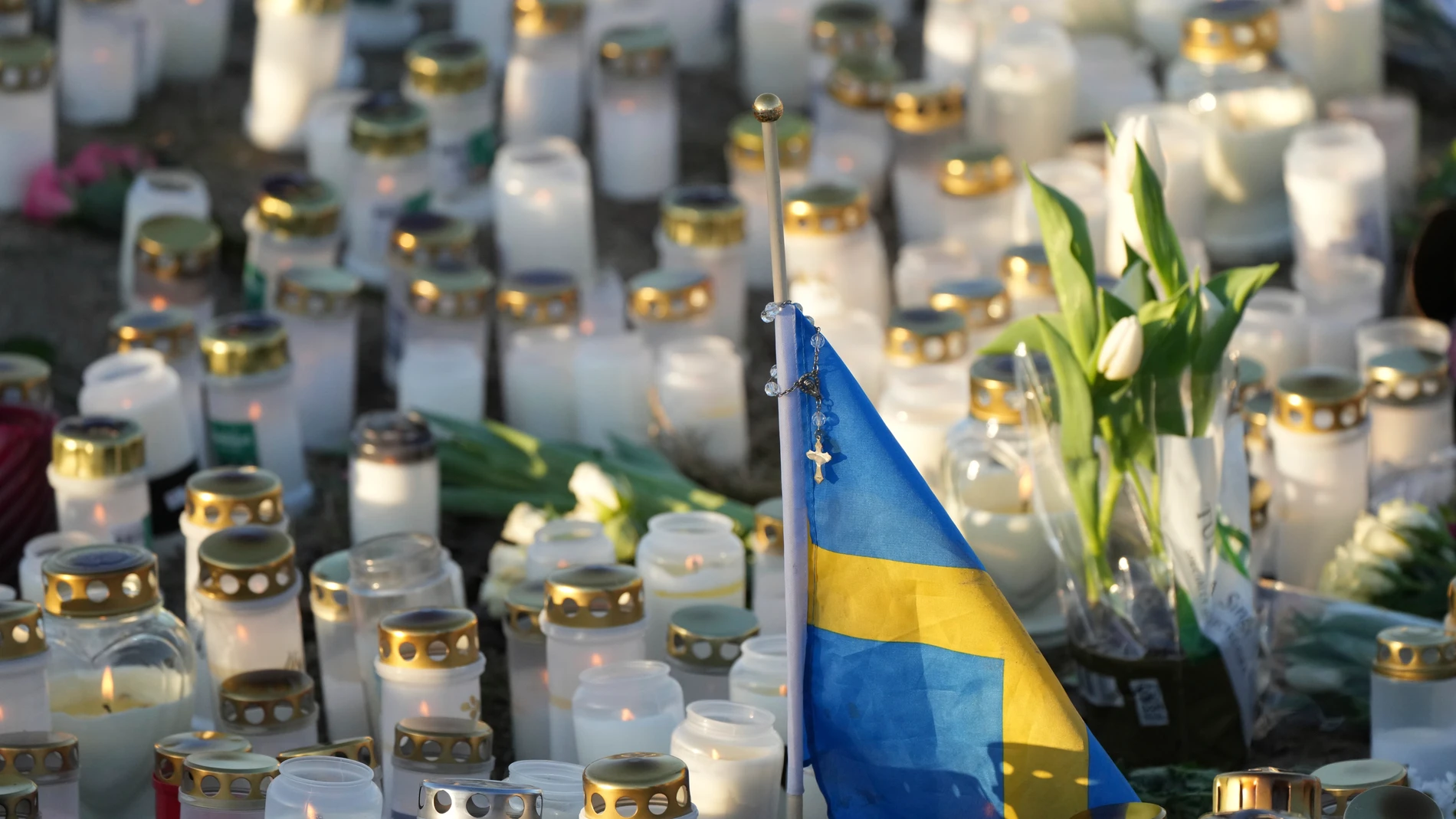 A Swedish flag is seen among candles and flowers at a makeshift memorial near the scene of a shooting on the outskirts of Orebro, Sweden, Friday, Feb. 7, 2025. (AP Photo/Sergei Grits)