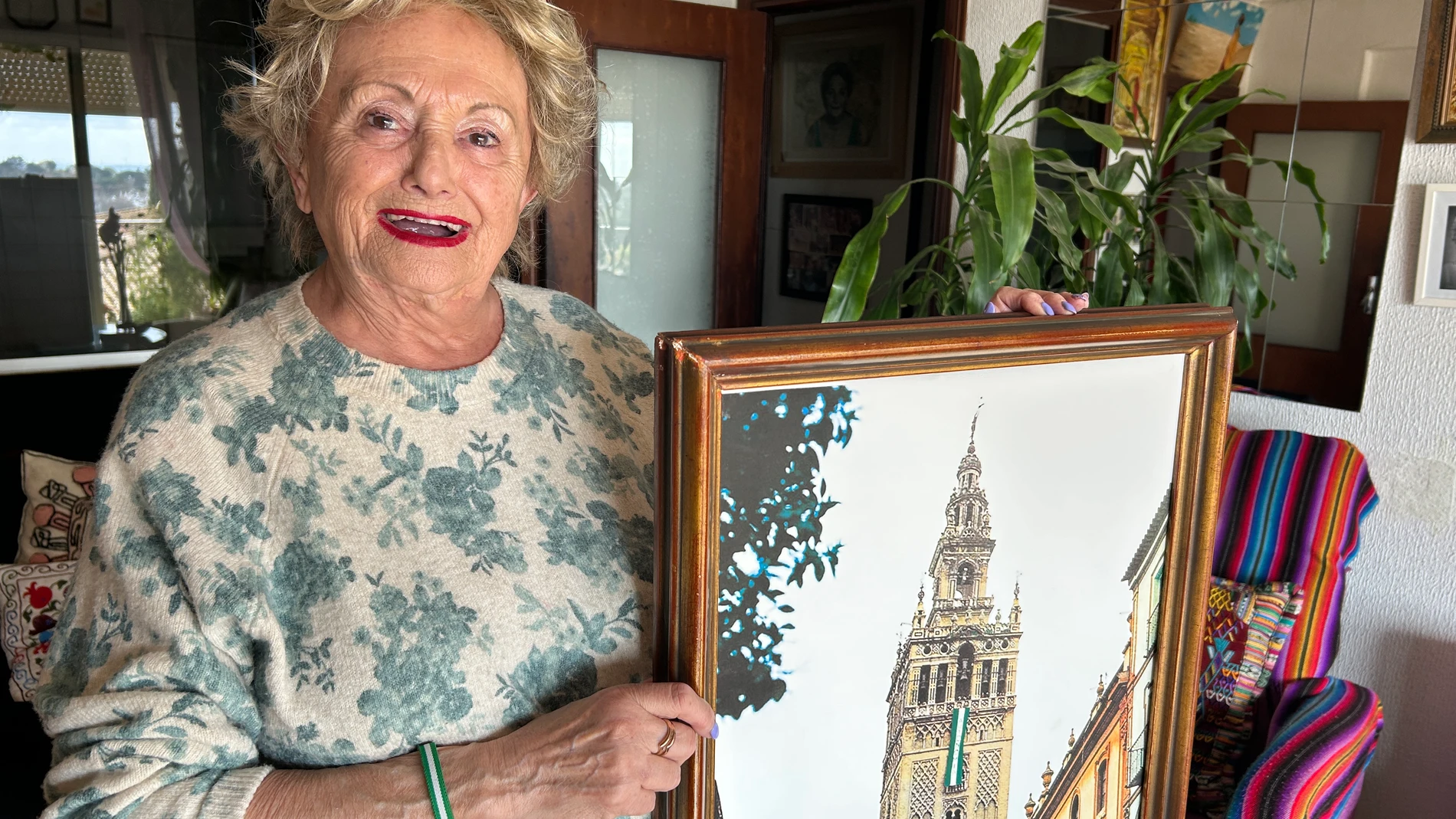 MAIRENA DEL ALJARAFE (SEVILLA), 28/02/2025.- Eligia Lorenzo, una de las fundadoras del Partido Socialista de Andalucía y a punto de cumplir 90 años, posa en su casa de la localidad sevillana de Mairena del Aljarafe con una fotografía en la que muestra la bandera de Andalucía de 12 metros que cosió y que colgaron clandestinamente de la Giralda de Sevilla para reclamar la autonomía en febrero de 1977. EFE/Fermín Cabanillas