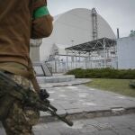 A Ukrainian soldier stands against the background of a shelter above the sarcophagus covering the exploded reactor at the Chernobyl nuclear power plant in Chernobyl, Ukraine, Saturday, April 16, 2022. (AP Photo/Efrem Lukatsky)