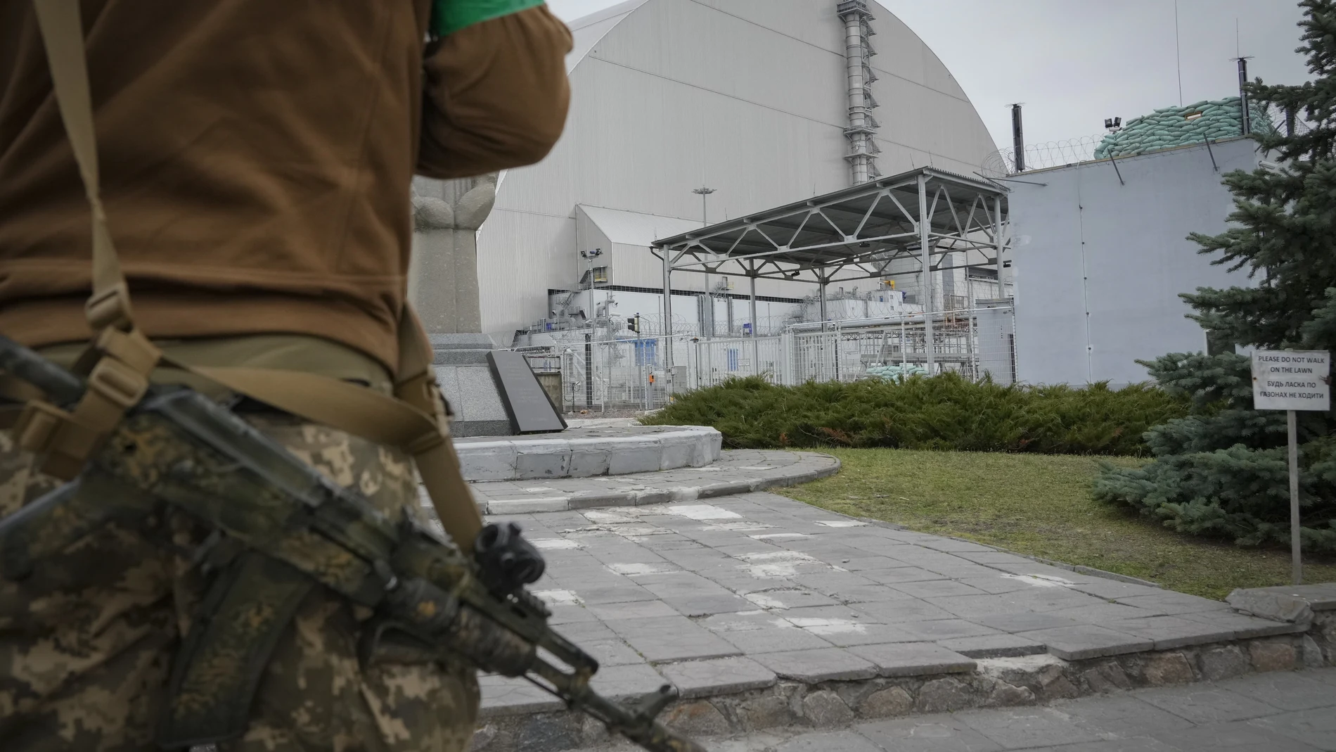 A Ukrainian soldier stands against the background of a shelter above the sarcophagus covering the exploded reactor at the Chernobyl nuclear power plant in Chernobyl, Ukraine, Saturday, April 16, 2022. (AP Photo/Efrem Lukatsky)