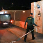 Un coche fúnebre y un agente de la Guardia Civil junto a la puerta donde tuvo lugar el suceso
