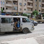Personas en un transporte público a lado de un vehículo militar vistas el 1 de mayo de 2025 en Sahnaya, a las afueras de Damasco, que ha recuperado una relativa calma tras los sangrientos enfrentamientos del miércoles. Vehículos calcinados a orillas de las carreteras, agujeros dejados por el impacto de las balas en las paredes de las casas y los cristales que se esparcen por las callesjuelas de Sahnaya 