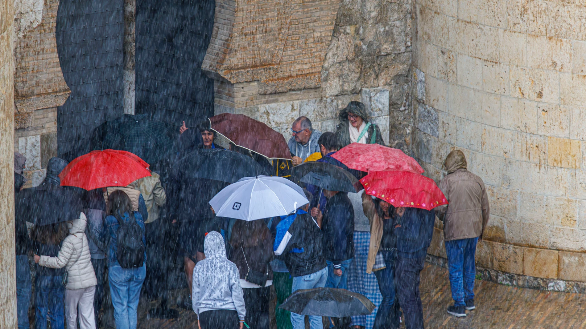 ZARAGOZA, 02/05/2025.- Turistas a las puertas del palacio de La Aljaferia se protegen del chaparrón de este viernes en Zaragoza. La Agencia Estatal de Meteorología (Aemet) ha activado para este viernes la alerta amarilla por lluvias intensas en la práctica totalidad del territorio de Aragón, que ha situado en naranja en las sierras turolenses por tormentas que podrían ir acompañadas de granizo y fuertes vientos. EFE/ Javier Belver