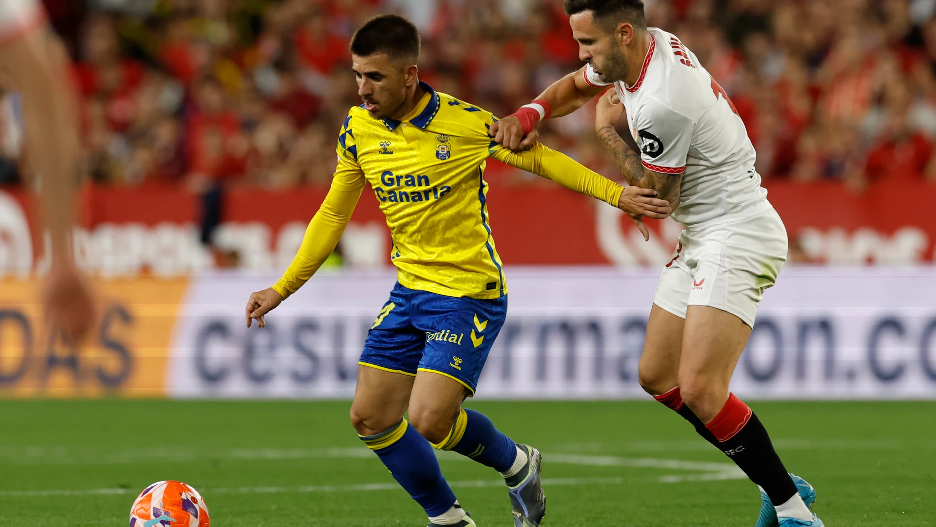 SEVILLA, 13/05/2025.- El centrocampista del Sevilla FC Saúl Ñíguez (d) lucha con Manu Fuster, de la UD Las Palmas, durante el partido de la jornada 36 de LaLiga que Sevilla FC y UD Las Palmas disputan este martes en el estadio Ramón Sánchez-Pizjuán. EFE/Julio Muñoz