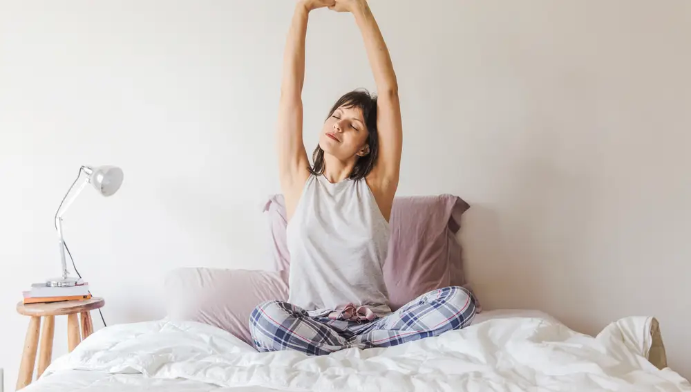Mujer estirando los brazos en la cama por la mañana