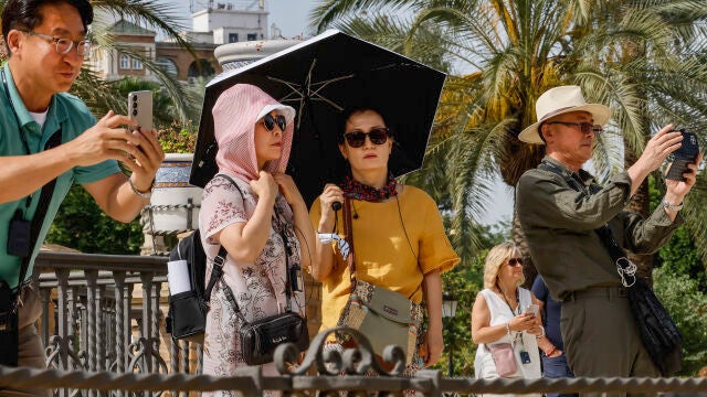 Turistas pasean protegidos con paraguas y pañuelos en la plaza de América de Sevilla