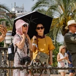 Turistas pasean protegidos con paraguas y pañuelos en la plaza de América de Sevilla