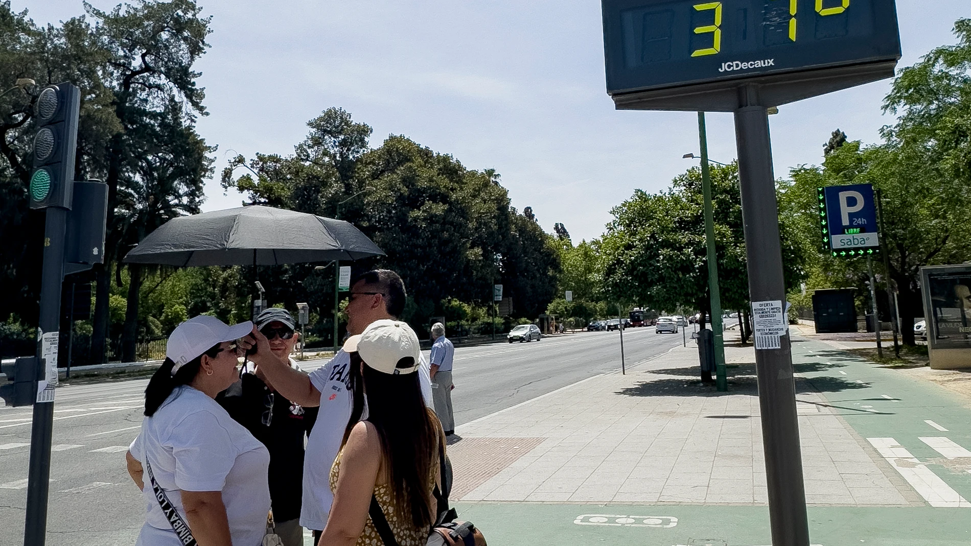 SEVILLA, 01/06/2025.- Varias personas conversa bajo un termómetro que marca 37 grados este domingo en Sevilla. EFE/David Arjona