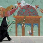 Una iraní cubierta con un velo pasa junto a un mural en una calle de Teherán