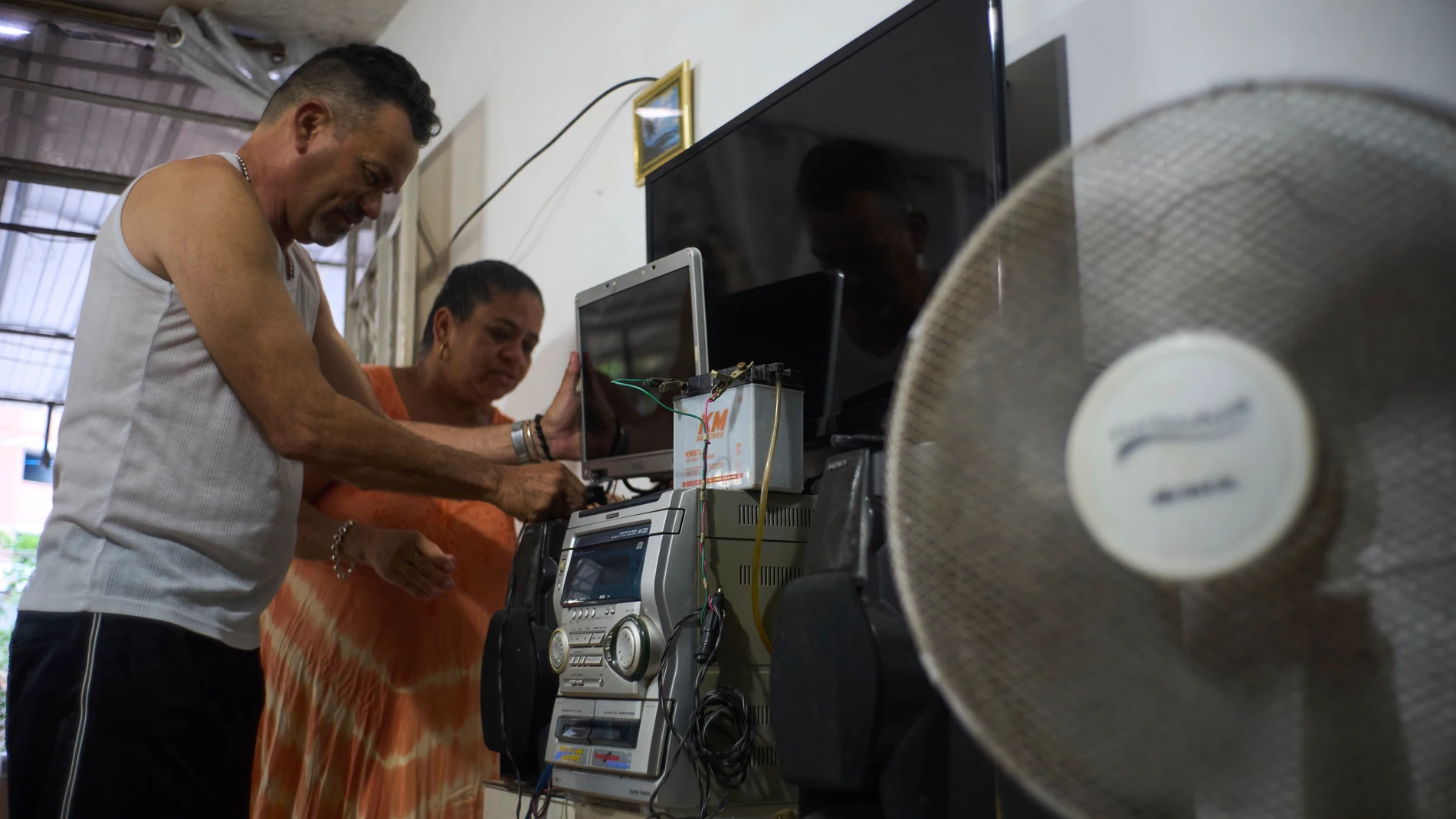 Married couple Angel Rodriguez and Marylin Alvarez set up a motorcycle battery to power a laptop screen to watch television, as they stay prepared for blackouts in the Bahia neighborhood of Havana, Cuba, Monday, May 26, 2025. (AP Photo/Ramon Espinosa)