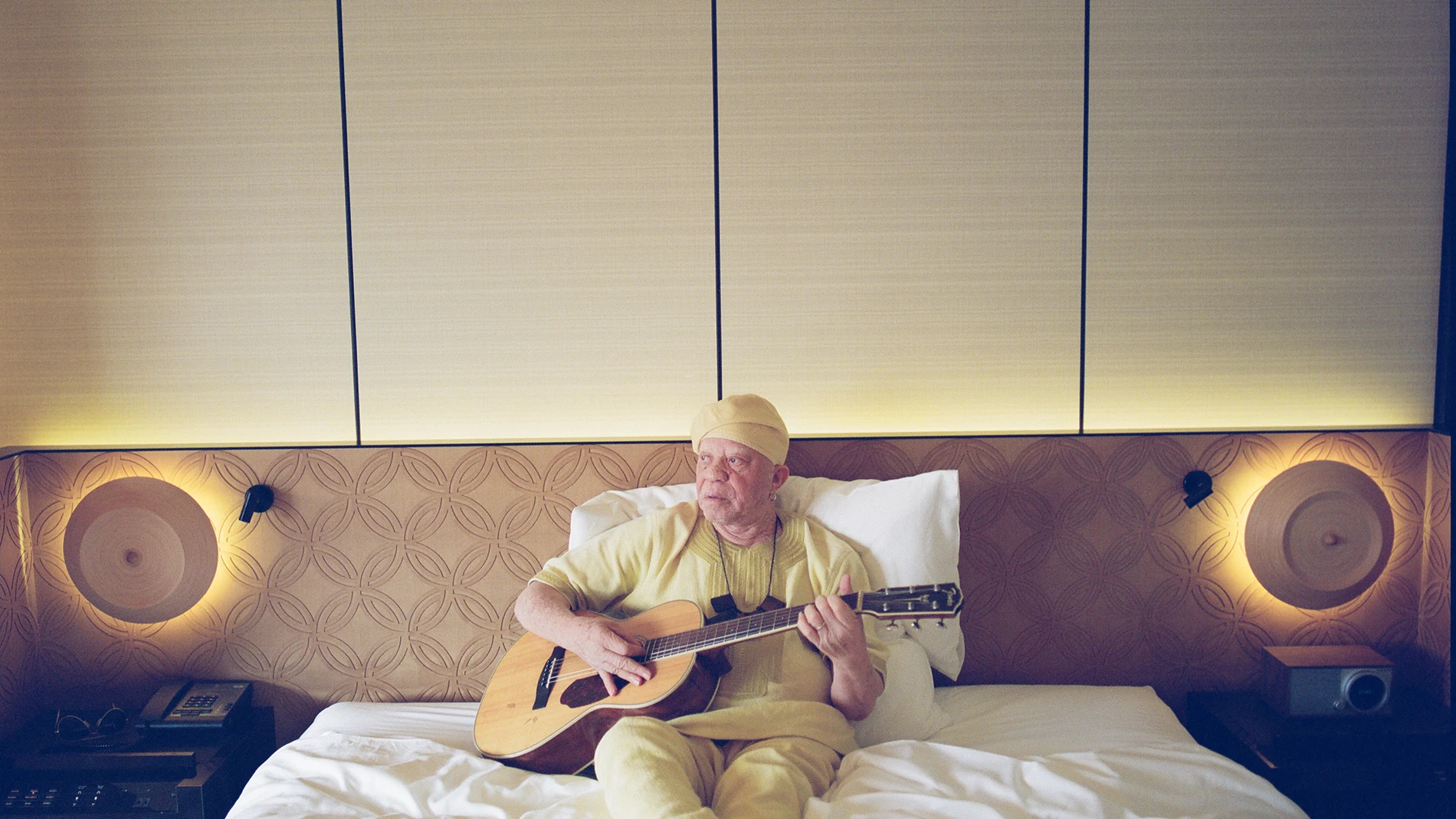 El músico maliense Salif Keita posa en una cama con su guitarra.