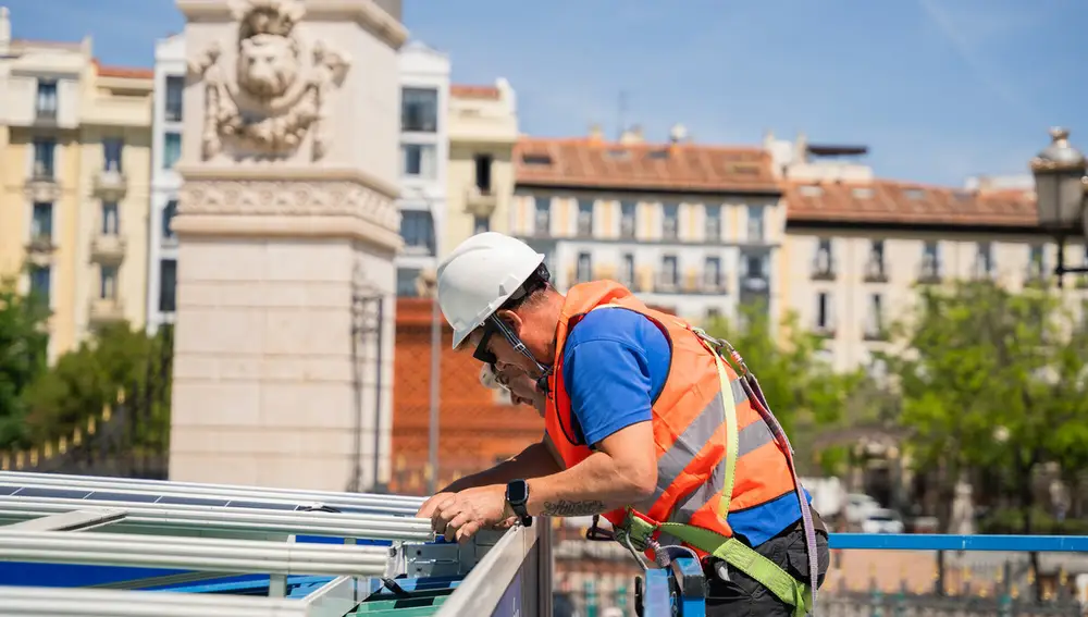 Dos técnicos instalan los paneles solares en el techo de las casetas de la Feria del Libro de Madrid
