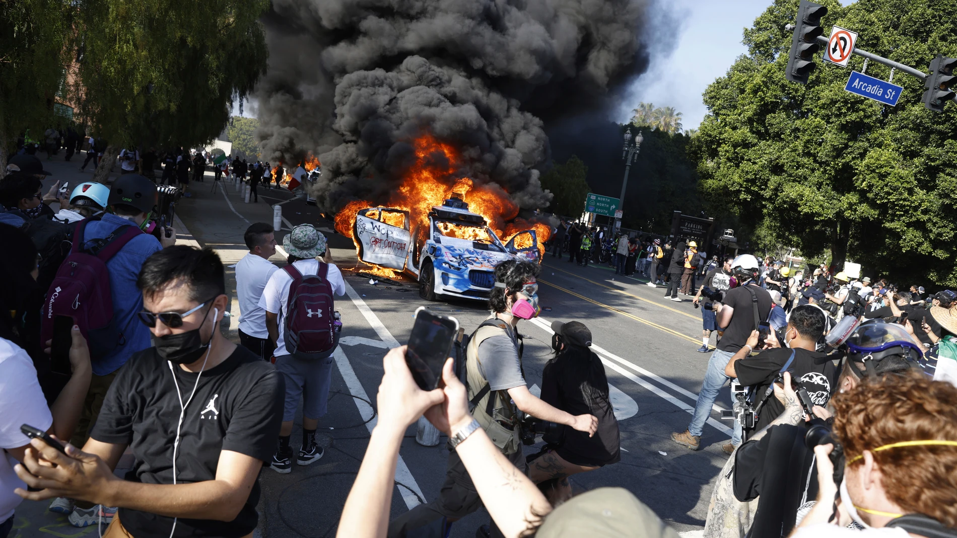 People watch while several Waymo cars burn in downtown Los Angeles after being vandalized by protesters reacting to a series of immigration raids that occurred in Los Angeles, Calif., on Sunday, June 8, 2025. (Stephen Lam/San Francisco Chronicle via AP)