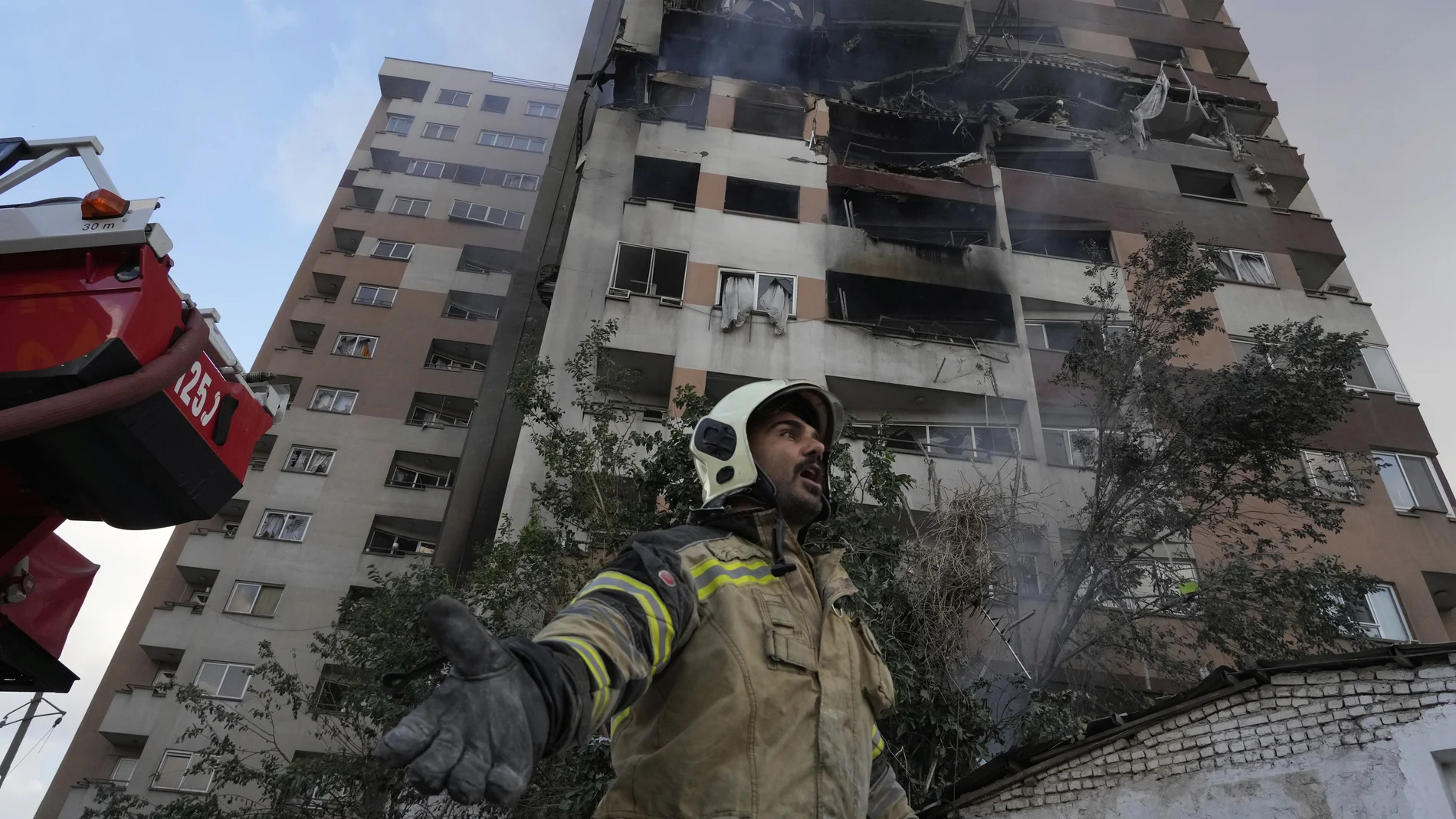 A firefighter calls out his colleagues at the scene of an explosion in a residence compound in northern Tehran, Iran, Friday, June 13, 2025.
