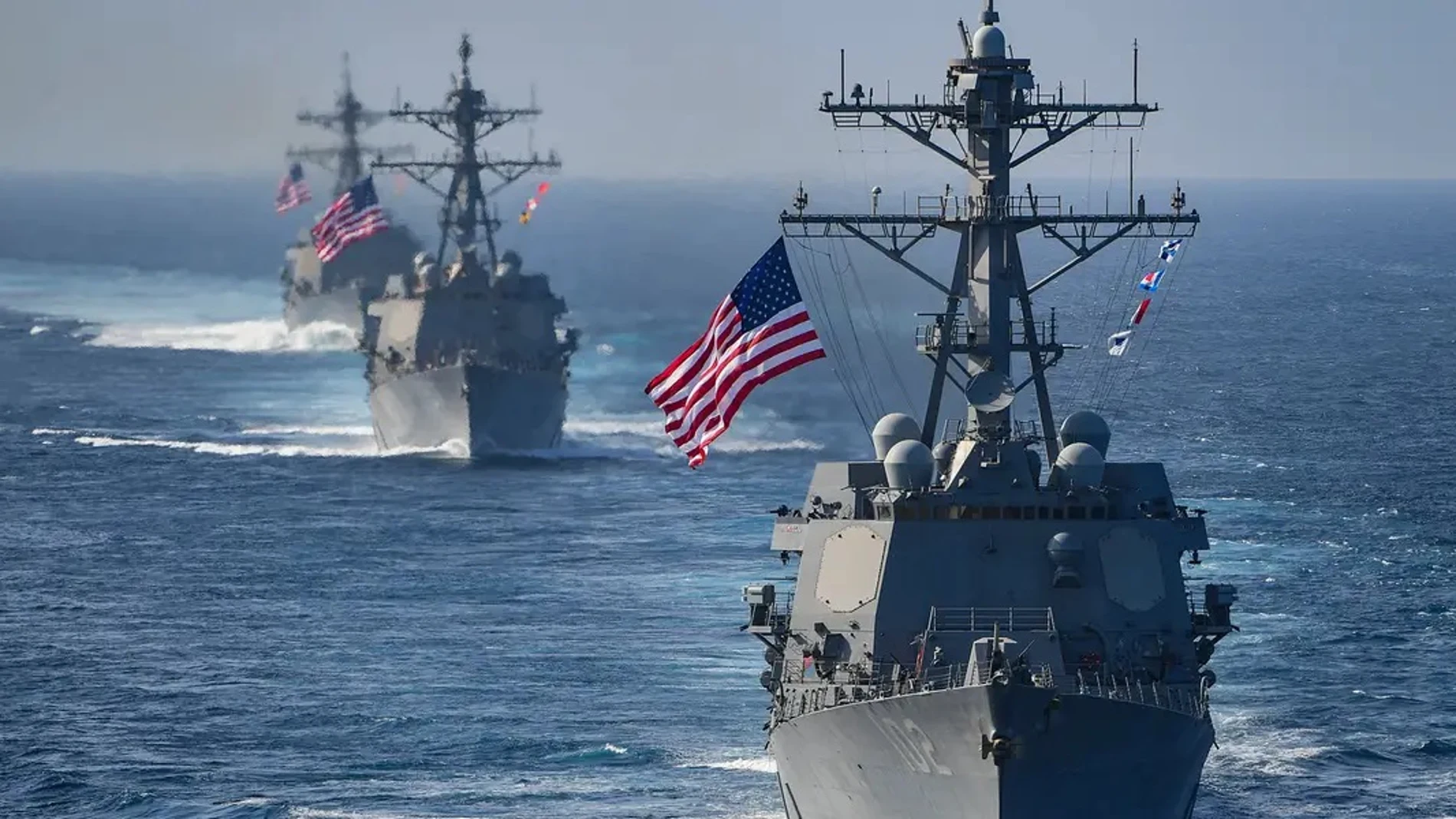 Tres barcos de la marina de Estados Unidos en sucesión uno detrás de otro enarbolando la bandera de su país