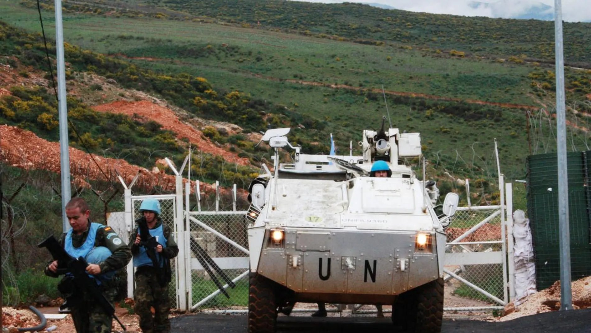 Aparece la entrada de una base militar con verjas en el que delante hay un vehículo blindado de transporte