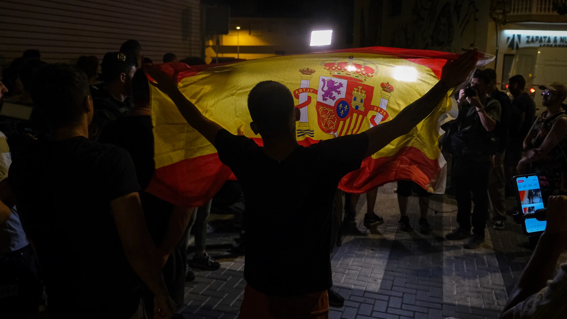 TORRE PACHECO (MURCIA), 15/07/2025.- Un manifestante ondea una bandera de España mientras increpa a periodistas este martes en Torre Pacheco (Murcia). La Guardia Civil ha impedido la manifestación prevista para las 20:00 horas a las puertas del Ayuntamiento de Torre Pacheco para evitar altercados ante la presencia de grupos ultra en la población. Según fuentes cercanas al instituto armado consultadas por EFE, los agentes están invitando a los asistentes a abandonar la zona, en la que se encon...