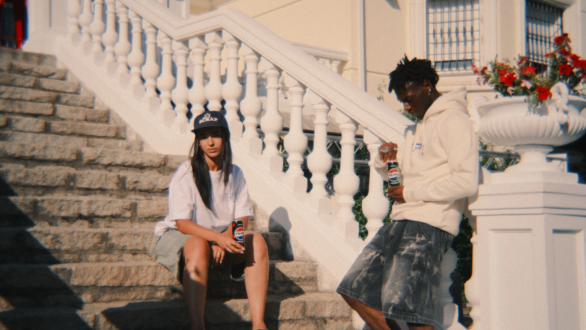 Imagen promocional de la colección cápsula Ndless Youth de Pepsi x ScrapWorld. Dos jóvenes posan con prendas de la línea en un entorno urbano y veraniego, con latas de Pepsi Zero Cherry y Pepsi Zero Lima en mano.