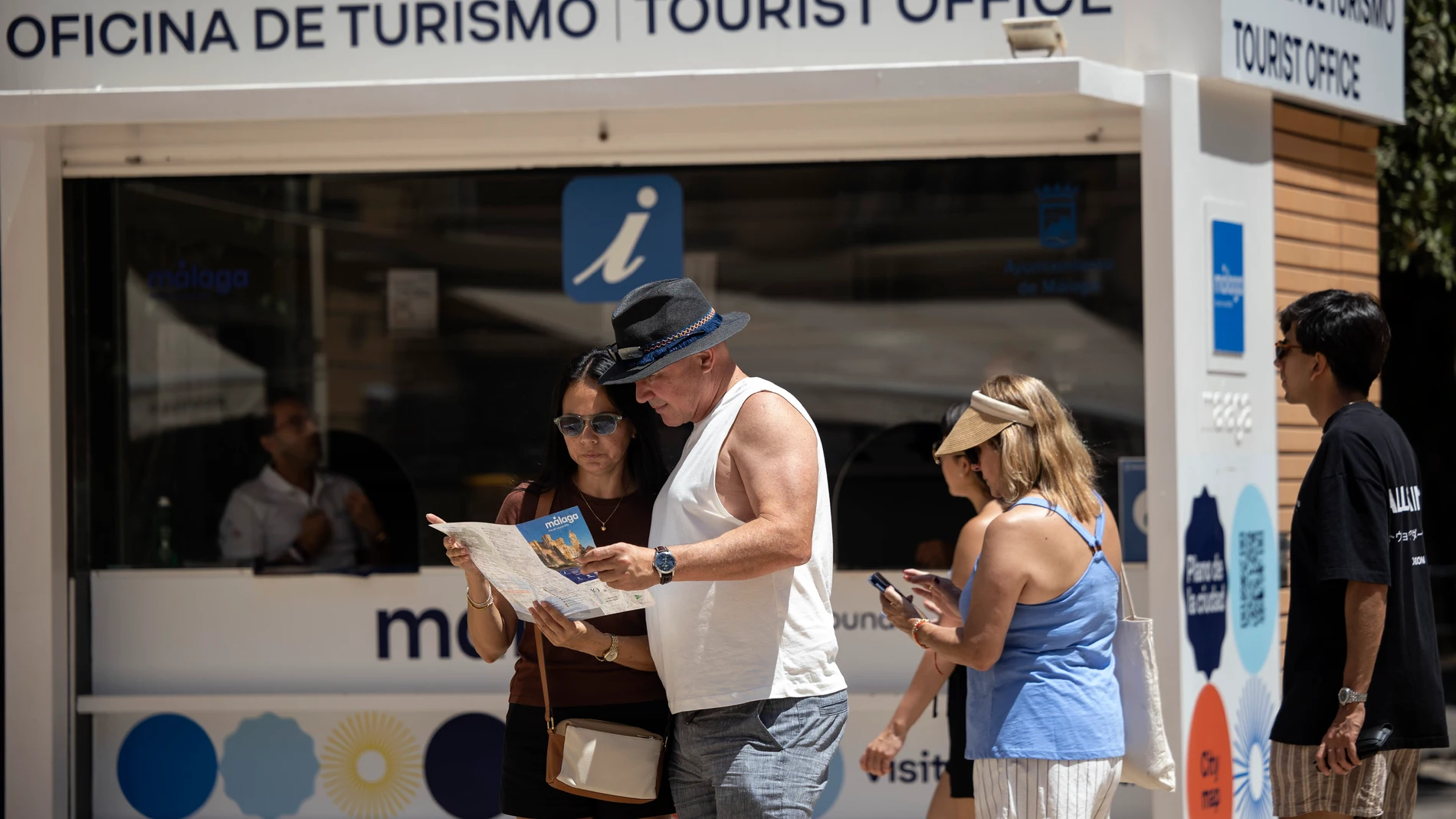 Varios turistas caminan por el centro de Málaga y piden información en la Oficina de Turismo de la ciudad en un día de calor sofocante
