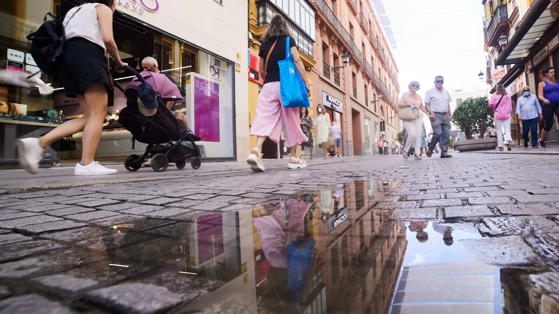 Personas reflejadas en un charco en Sevilla