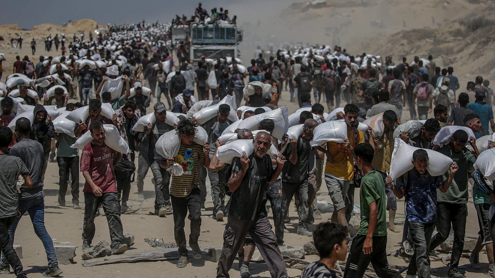 ZIKIM (-), 27/07/2025.- Internally displaced Palestinians carry bags of flour near a food distribution point in Zikim, northern Gaza Strip, 27 July 2025. The Israeli army declared a 'tactical pause' in military operations in parts of the Gaza Strip on 27 July, to facilitate the safe passage of humanitarian aid convoys. More than 130 Palestinians, the majority of whom children, have died of malnutrition in the Gaza Strip, the Palestinian Ministry of Health said on 27 July. EFE/EPA/MOHAMMED SABER