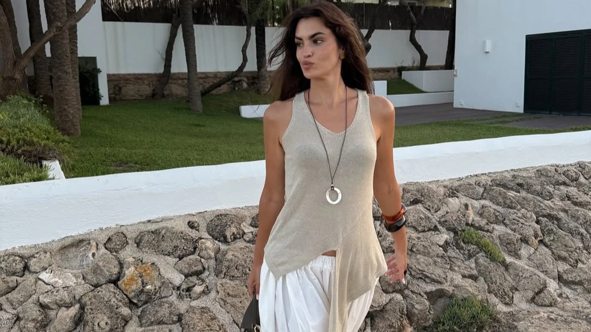 Marta Lozano con pantalón bombacho blanco, top drapeado en tono neutro y bolso estructurado, en un look veraniego y relajado.