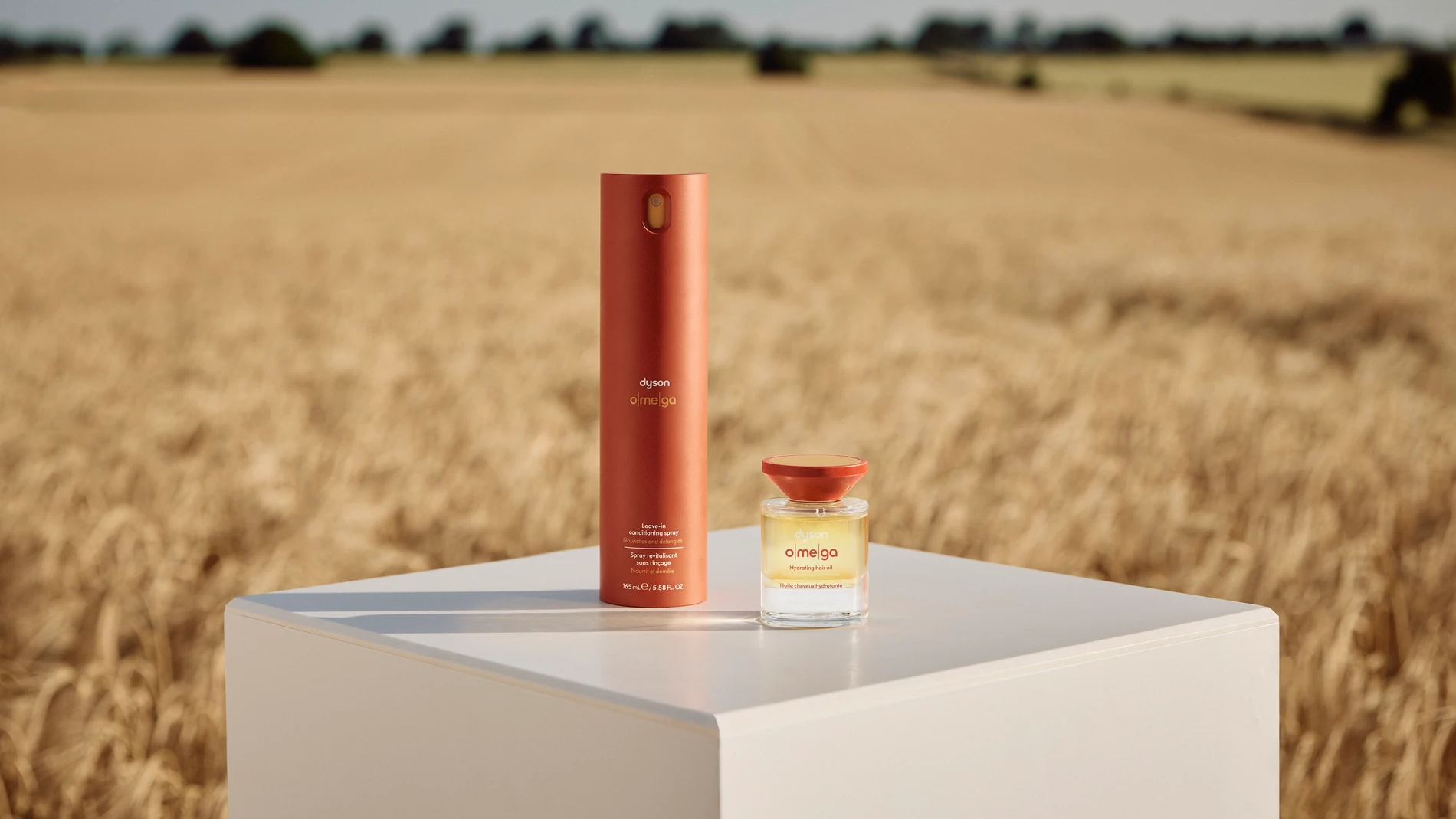 Fotografía de los productos de la gama capilar Dyson Omega™ (aceite hidratante y spray acondicionador) sobre base neutra