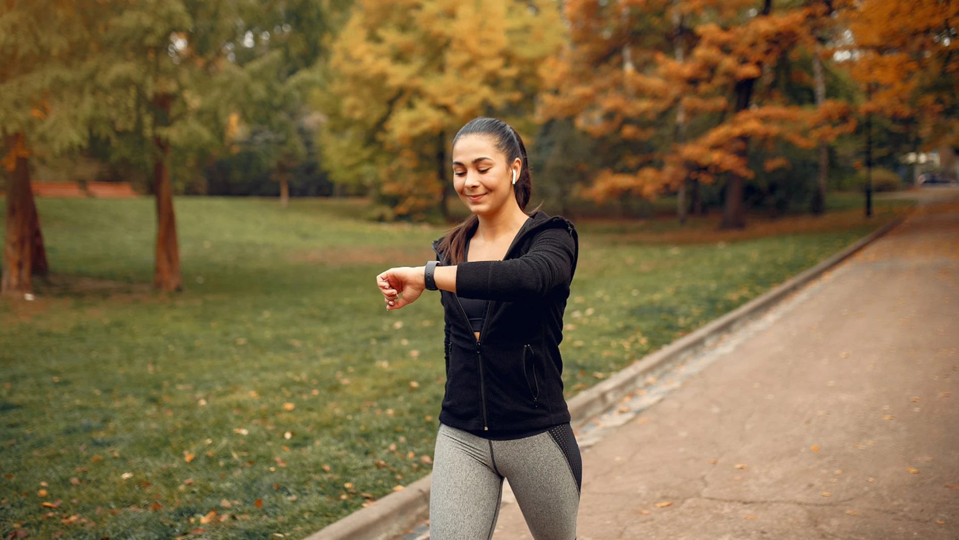 Mujer joven caminando al aire libre en un parque usando smartwatch para contar pasos diarios