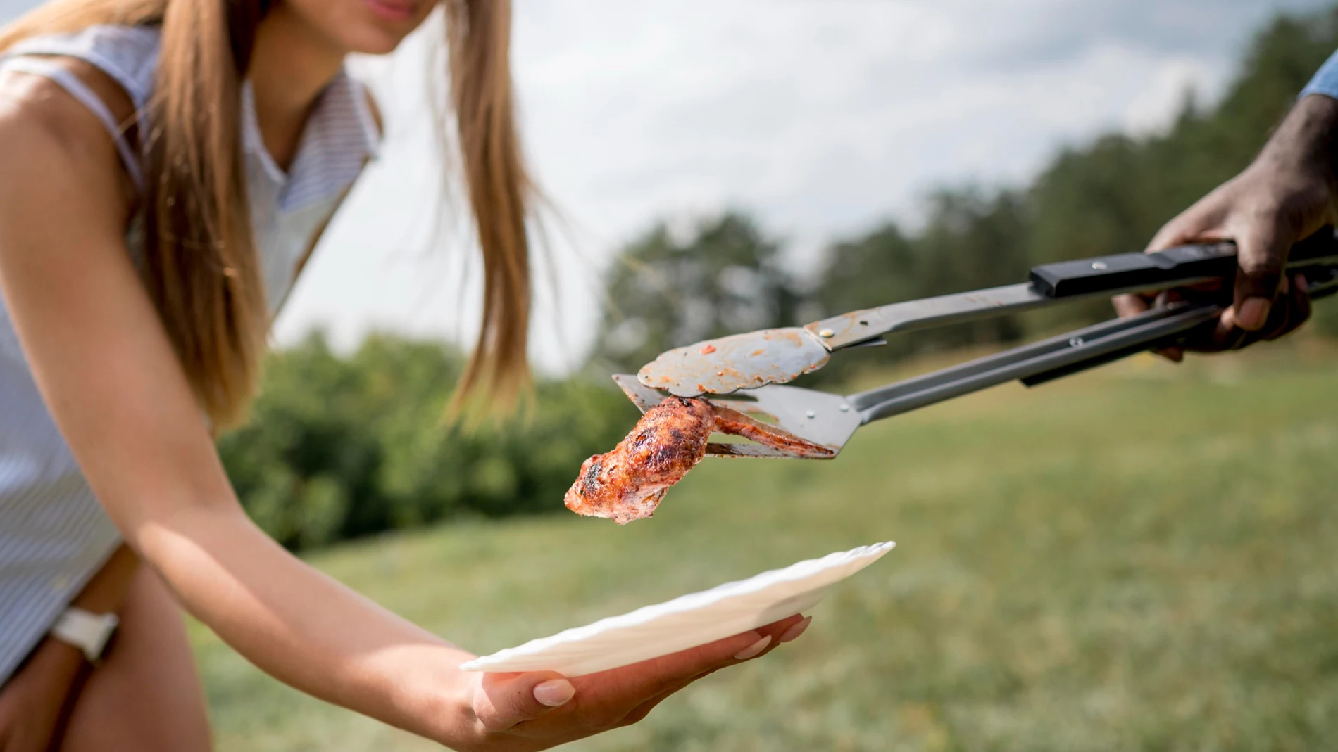 Muslo de pollo a la brasa en barbacoa de amigos sobre plato mujer joven