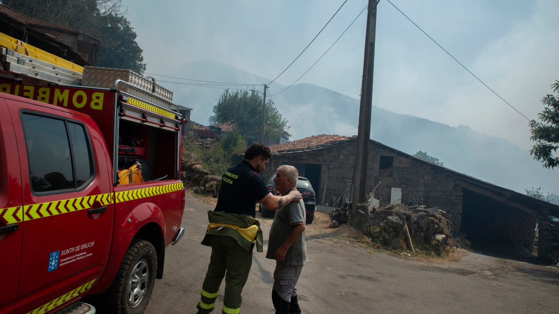 Un residente y un bombero después de la noche con el fuego alrededor de la aldea, a 10 de agosto de 2025, en Maceda, Ourense, Galicia (España). Un incendio en Maceda (Ourense), parroquia de Castro de Escuadro, calcina más de 20 hectáreas desde su inicio a las 23.19 horas del sábado. Se inició en cinco o seis puntos casi simultáneos, según informa la Consellería do Medio Rural, que por este motivo ve una clara intencionalidad en él. Fue necesaria decretar la Situación 2 esta madrugada por la p...