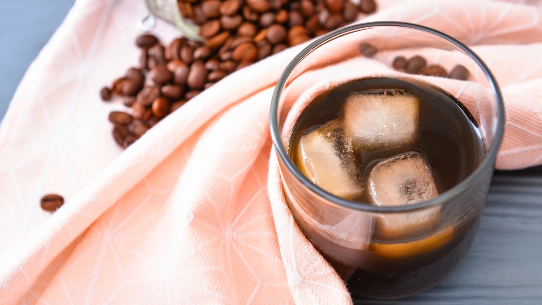 Vaso de café negro solo con hielo sobre mantel de verano con granos de café
