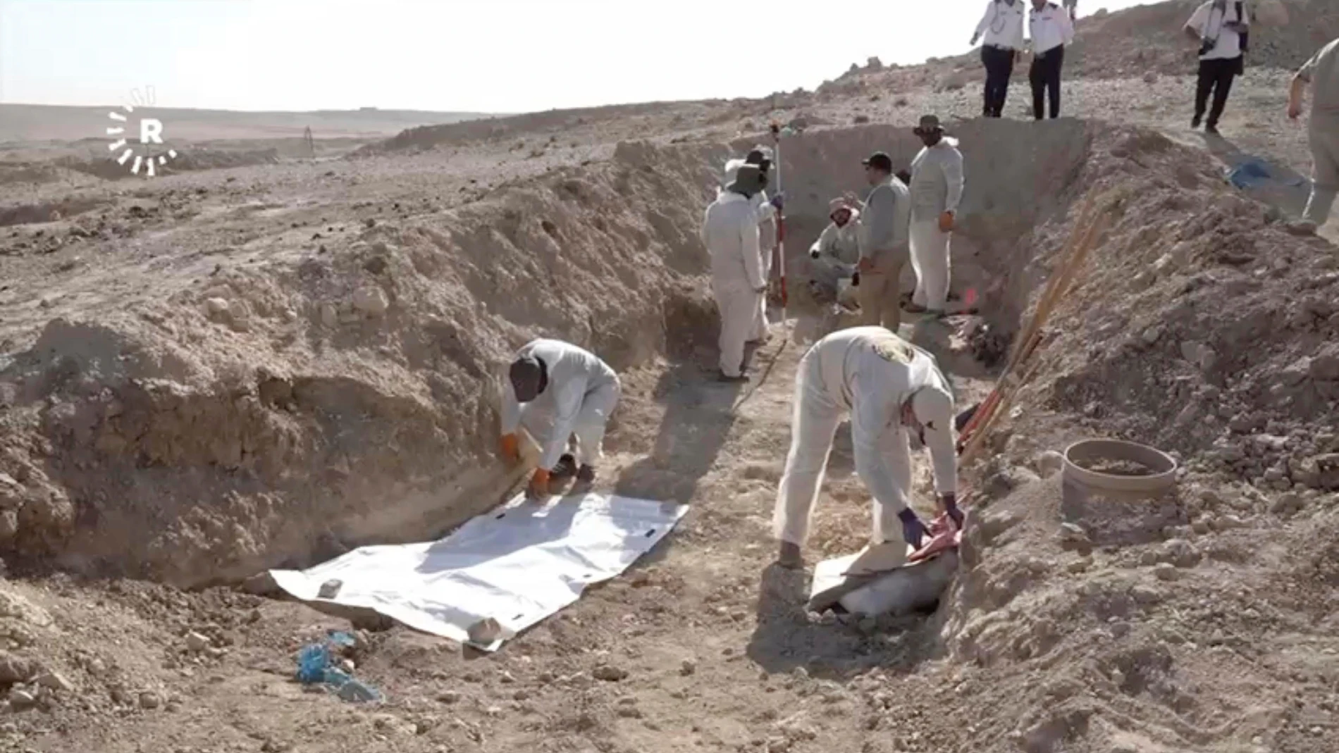 In this image taken from video provided by Rudaw TV, workers dig out human remains at the Khasfa site near the northern Iraqi city of Mosul, where authorities have begun excavating a mass grave believed to contain thousands of victims of the Islamic State (IS) Mosul, Iraq, Sunday, Aug. 17, 2025. (Rudaw TV via AP)
