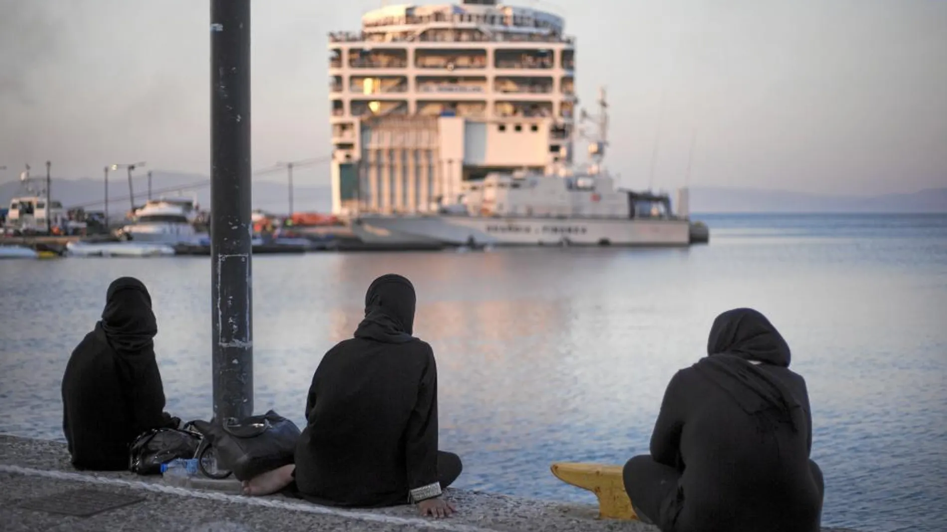 Tres mujeres observan desde la costa el crucero amarrado en la isla de Kos.