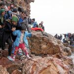 Un grupo de inmigrantes escala por las rocas tras llegar ayer en un inseguro bote a la isla griega de Lesbos