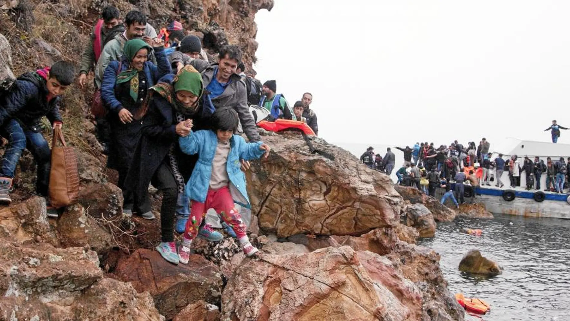 Un grupo de inmigrantes escala por las rocas tras llegar ayer en un inseguro bote a la isla griega de Lesbos