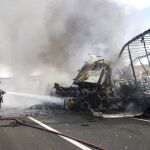 Dos bomberos intentan sofocar el fuego que se ha producido en el accidente de dos camiones articulados, cuyos conductores han fallecido