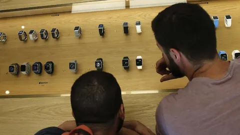Dos hombres observan varias unidades del reloj inteligente de Apple, Apple Watch, que ha salido a la venta hoy en España.