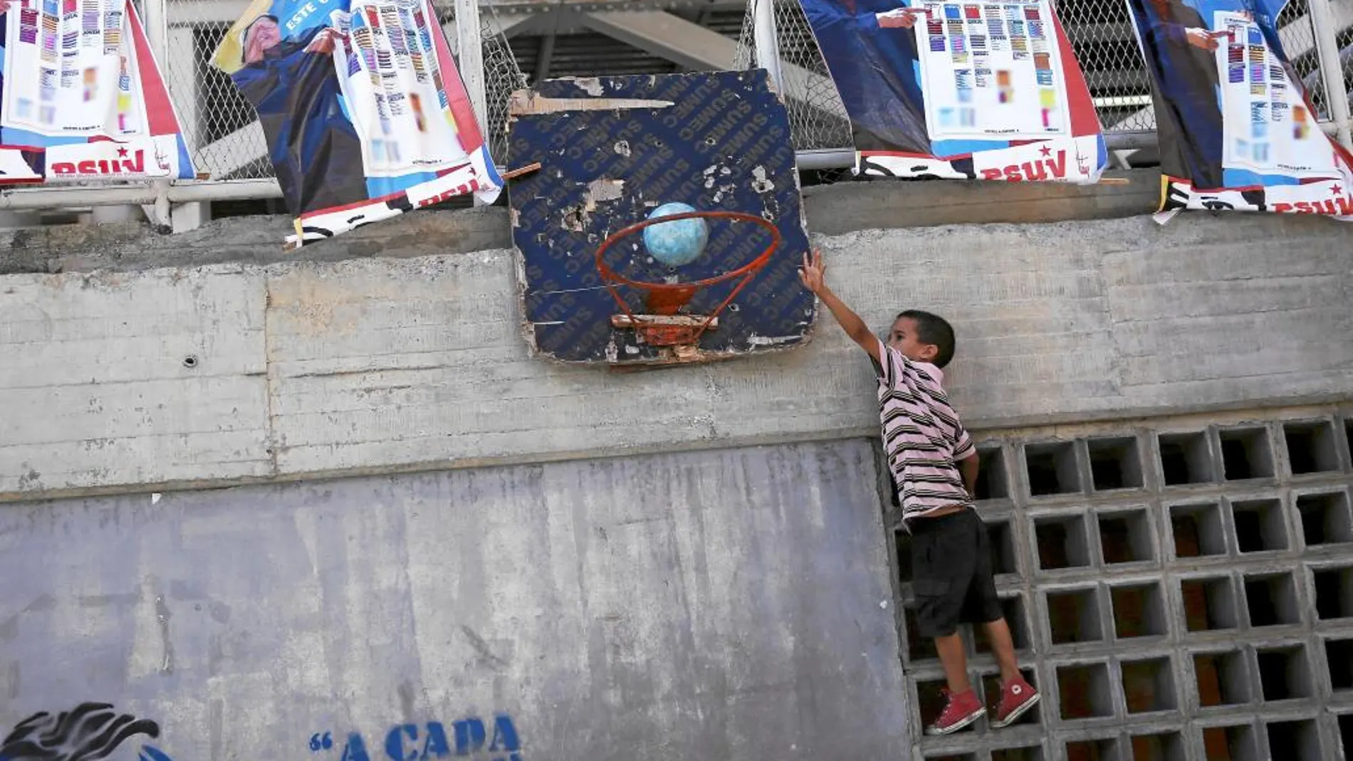 Un niño juega al baloncesto en una cancha plagada de pósters con el rostro de Hugo Chávez, en Caracas